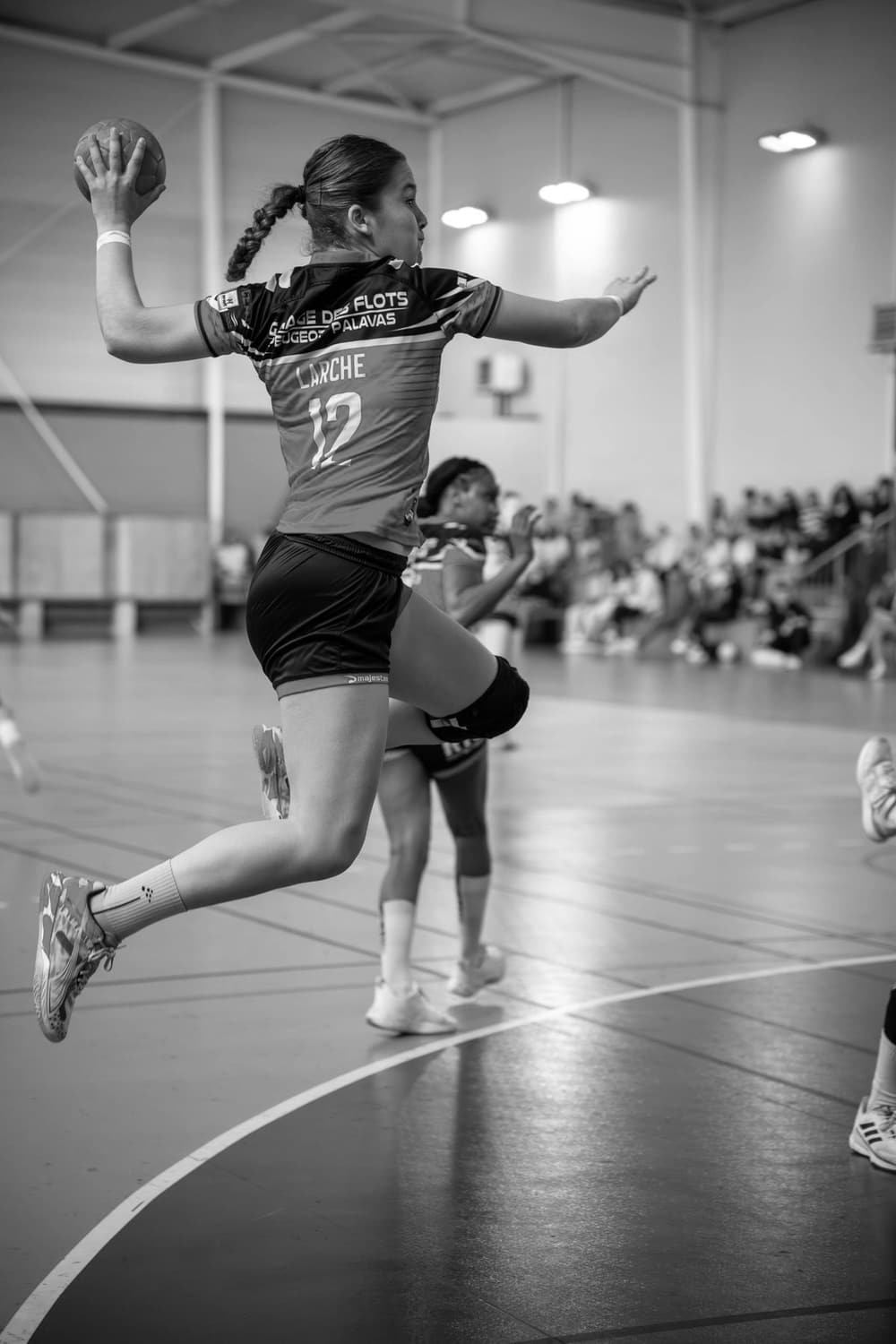 A handball player in mid-air with the ball drawn back overhead for a jump shot in a sports hall.