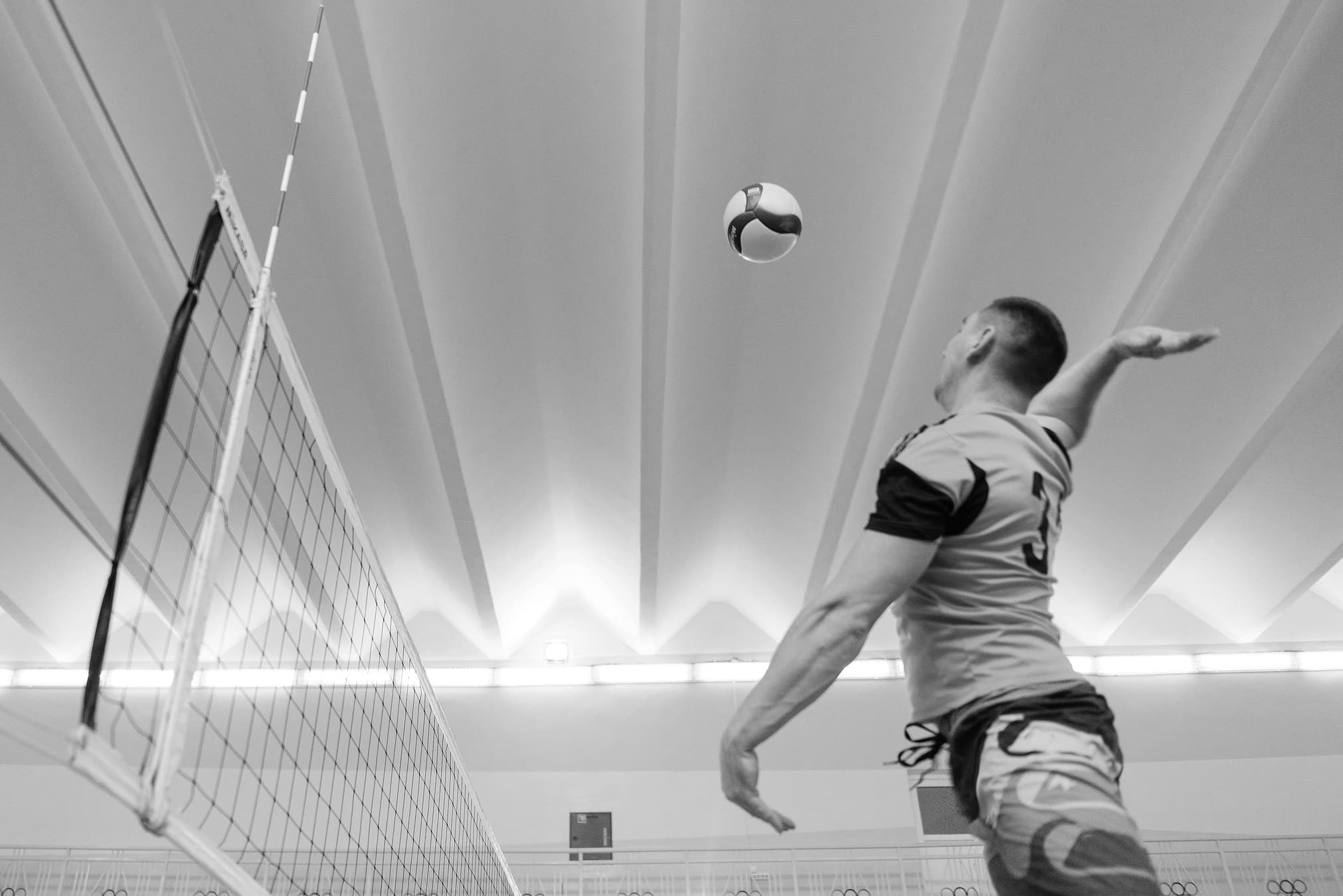 A volleyball player at the top of his jump, arm drawn back to spike, in a sports hall.